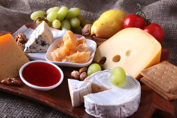 Assortment of cheese with fruits, grapes and nuts on a wooden serving tray.