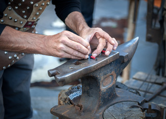 Blacksmith working the metal on Anvil in the foreground.