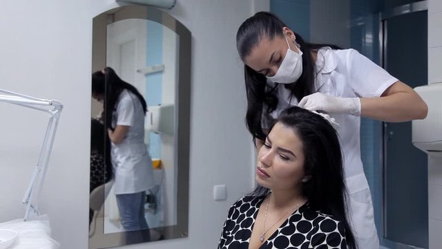 In the beauty salon the cosmetologist makes injections into the skin of the girl's head in order to improve the condition of the hair. Procedure of mesotherapy of hair