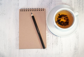 Notepad for notes or for sketches on a wooden table. Near the black pencil and cap of tea.