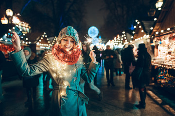 Outdoor photo of young beautiful happy smiling girl holding sparklers, posing in street. Festive...