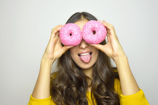 Close-up portrait of funny smiling girl with donuts isolated on gray background. Attractive young woman with long hair posing with sweets in her hands