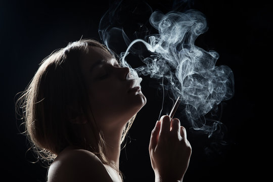 young woman smoking cigarette on black background