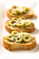 Obraz na płótnie Canvas Crostini with green olive slices and freshly grated parmesan-like hard cheese, photographed with natural light (Selective Focus, Focus in the middle of the first crostini)
