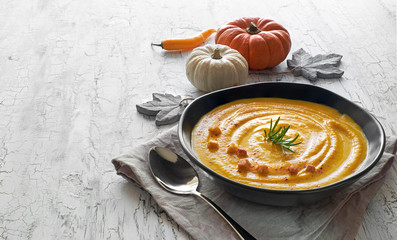 Spicy pumpkin soup with chili served in black ceramic plate om rustic background