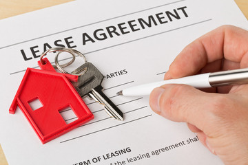 Man holding pen over house door key with red keychain pendant and lease agreement form