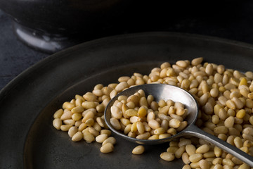 Heap of raw, uncooked pine nuts in metal spoon