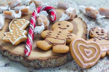 Fototapeta na wymiar Sweet gifts for holiydays. Homemade christmas gingerbread cookies and caramel candies on wooden board, horizontal