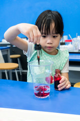 Kindergarten girl using droplet to add red color into a cup on blue table.