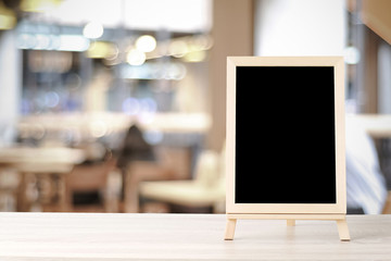 Blank chalkboard standing on wood table over blur restaurant with bokeh background, space for text, mock up, product display montage
