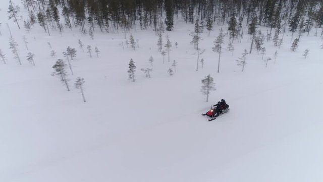 AERIAL CLOSE UP: People driving snowmobile on beautiful white snowy mountain slope exploring Lapland, Finland. Tourists on snowmobile adventure ride in spruce woods. Snowmobiling on witer wacations