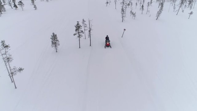 AERIAL, CLOSE UP: Unrecognizable couple riding snowmobile and competing on competition. Sportsmen speeding on snow vehicle along the track through snowy forested mountain. Snowmobiling in Finland