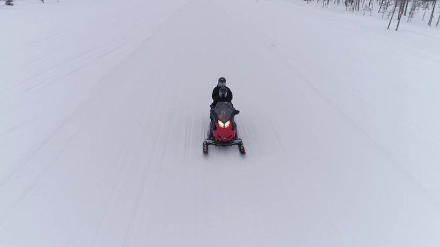 AERIAL CLOSE UP: People driving snowmobile on beautiful snowy mountain slope exploring Lapland countryside, Finland. Tourists on snowmobile adventure ride in forested winter wonderland. Snowmobiling