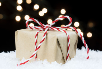 Handmade paper wrapped vintage gift tied in red and white twine sitting on snow