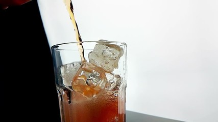 pouring orange drink alcohol cocktail into the glass with ice cubes on black background, slow motion