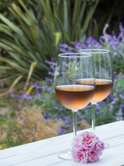 Two glasses of rosé with pink flowers, plants in background