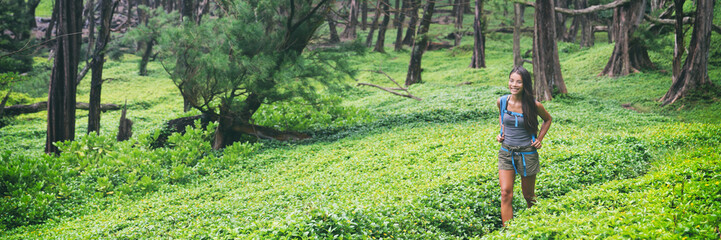 Nature hike travel hiking girl walking in lush forest landscape panorama. Happy Asian hiker woman on trail path in green grass. Panoramic banner.