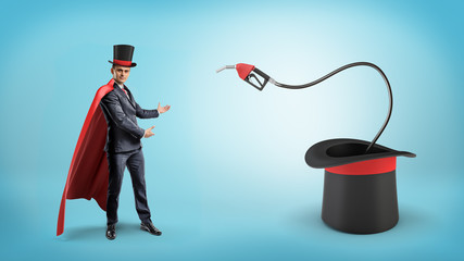 A businessman wearing a red cape and a big illusionist's hat shows a fuel nozzle inside a large...