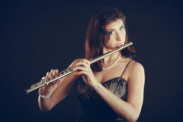 Woman playing transverse flute on black.