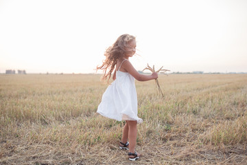 Little beautiful smiling girl on a gold wheat field walking at sunset. Happy five years old girl...