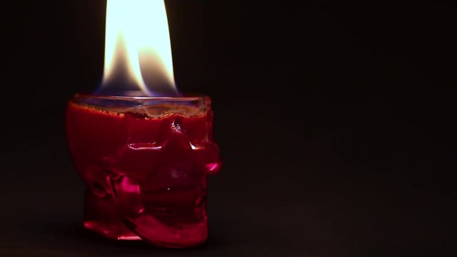 The fire burns in the glass-skull with a red liquid on a dark background. Footage for the Halloween party or a mystical extrasensory story.