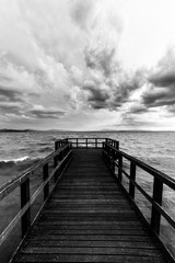 First person view of a pier on a lake on a moody day, with dark water and overcast, stormy sky