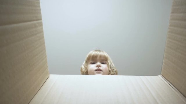 A little boy looks in the box, is surprised and happy to receive a surprise. The child opened a box with a gift. Slow Motion.