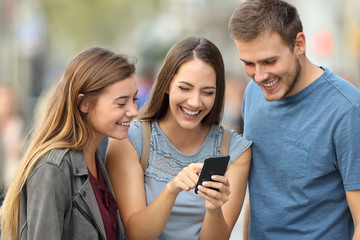 Three friends checking smart phone content on the street