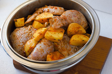Raw chicken legs with raw potatoes with spices for baking on a wooden table. Meat ingredients for cooking