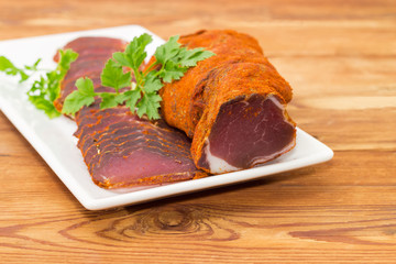 Partly sliced cured pork tenderloin on white dish closeup
