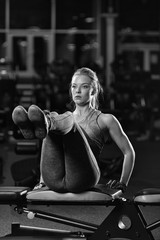 Woman doing strength exercises for abdominal muscles at indoor sport gym. Girl doing yoga stretches after running. Fitness model in dark sport club. Black and white.