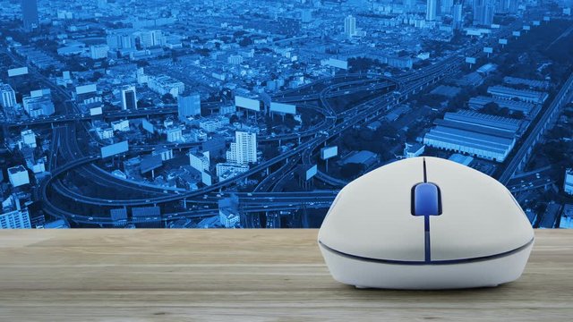 Taxi car flat icon with wireless computer mouse on wooden table over aerial of city tower, street and expressway, Internet business service taxi car concept