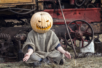 Jack-lantern with a pumpkin on his head meditates near a tractor.