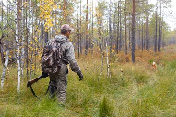 Papier Peint photo Chasser chasseur en tenue de camouflage avec fusil de chasse marchant dans la forêt