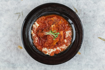 Top view of Pork rib chops steaks boiled with tomato sauce and cheese served in black round plate on washi (Japanese paper).