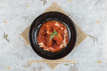 Top view of Pork rib chops steaks boiled with tomato sauce and cheese served in black round plate with chopstick  on makisu (meal mat).