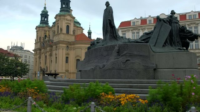 Camera slides past flowers with Jan Hus Monument and St Nicholas Church in the background. Prague