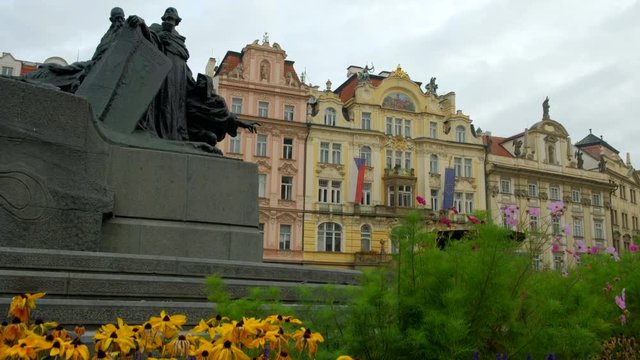 Camera rises from flower beds to reveal Jan Hus Monument and ornate buildings in Old Town Square, Prague