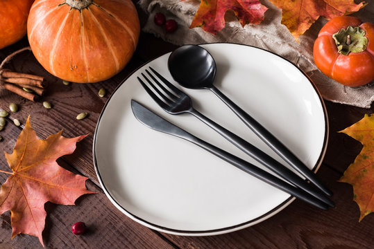 Thanksgiving table setting with pumpkins, wheat, fallen leaf and black cutlery