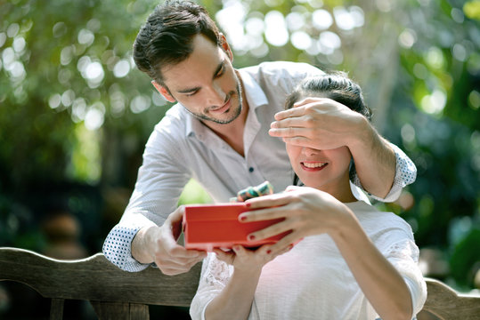 Young man is covering his girlfriend eyes and giving her a present