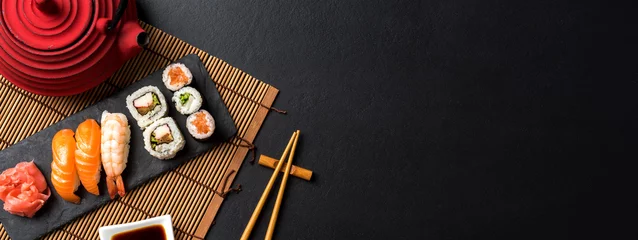 Fotobehang Sushi bar Set sushi met wasabi, sojasaus en theepot op zwarte stenen achtergrond