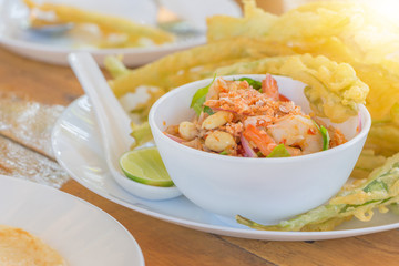 Deep fried morning glory with spicy shrimp salad on white plate and lemon on spoon, Thai food concept.
