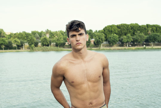 Retrato de medio cuerpo de hombre joven con el torso desnudo. De fondo, una zona llena de &aacute;rboles frondosos y un r&iacute;o.