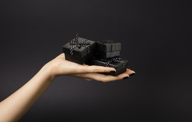 Female hand holding a three black gift boxes on a palm. Isolated on black background. Shallow depth...