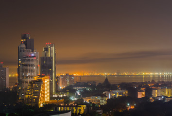 Fototapeta premium Night cityscape of skyline, tall buildings and cities near sea or river with gold and dark sky for copy space