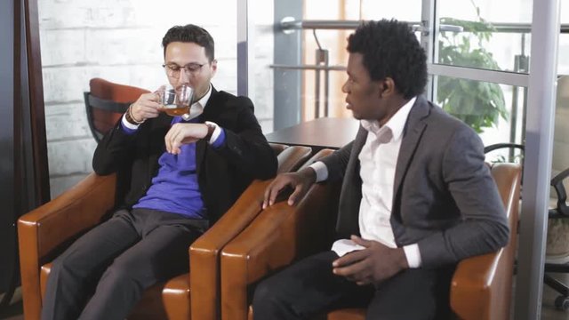 European man and African American man sitting in armchairs and negotiate