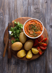 Young potatoes boiled in a peel with zucchini caviar or dip of vegetables, spices, fresh tomatoes and parsley on a wooden board. Simple healthy homemade food