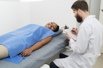 Female Patient Lying On Bed While Doctor Holding Clipboard