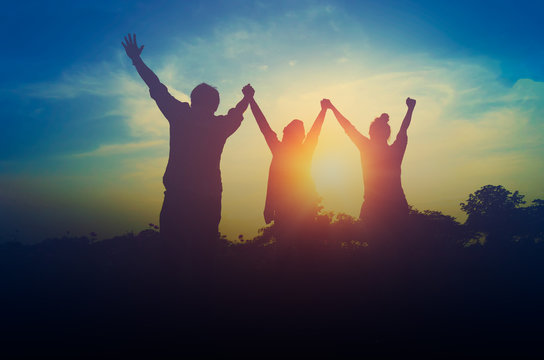 Silhouette of happy teamwork hold hands up as a business successful, business victory