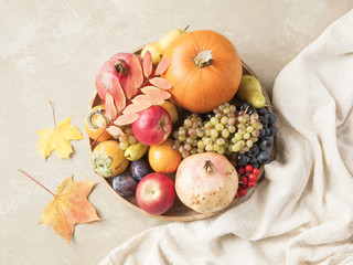 Obraz na płótnie Canvas Autumn food concept. Fruits, vegetables and nuts on wooden round tray on light brown background.